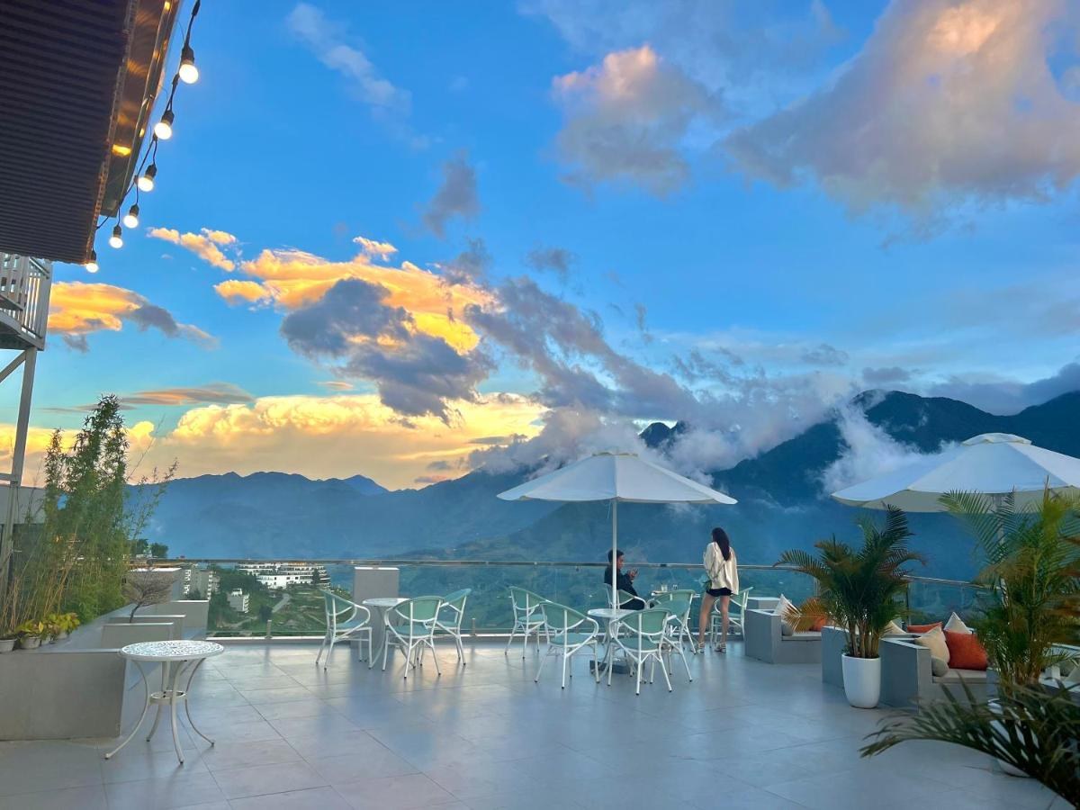 Open rooftop terrace with white tables and parasols, cloud lying along a mountain range at sunset