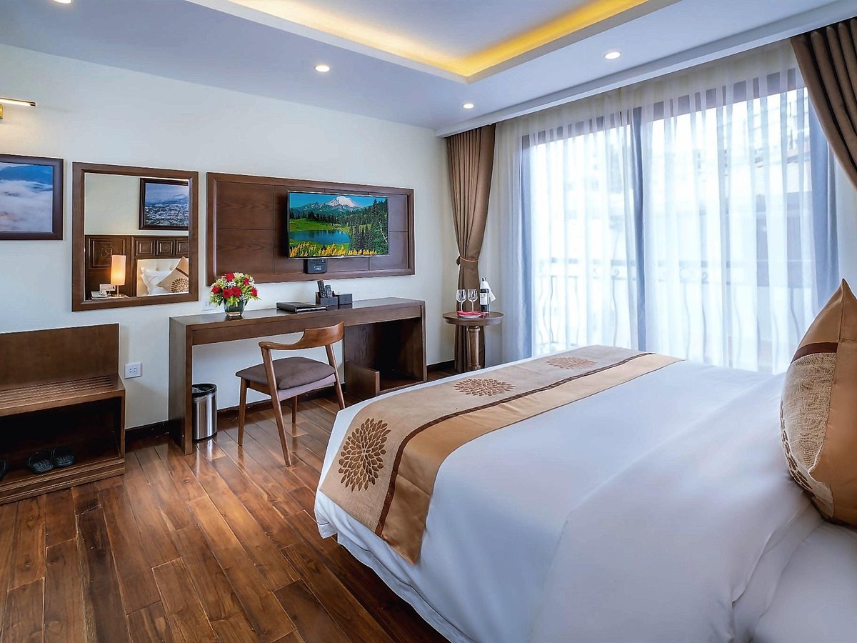 Double bed with a carved headboard runner, a wooden desk and chair and a curtained window