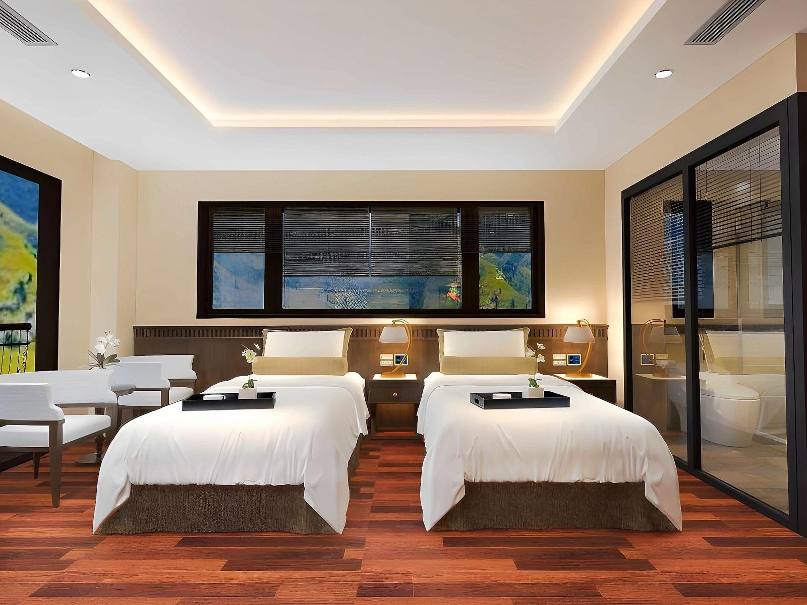 Twin room with two white beds, a long low headboard, white armchairs and a glass-walled bathroom