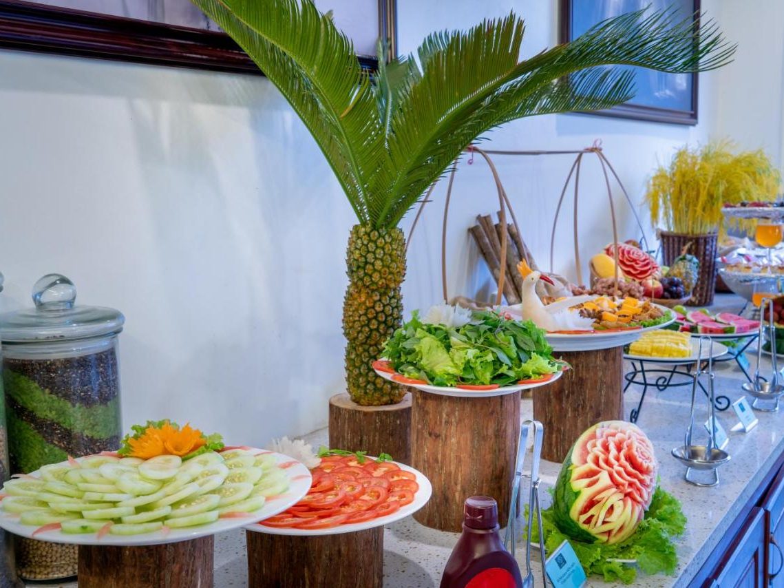 Breakfast buffet counter with carved watermelon, a pineapple palm, salads and sliced cucumber and tomato on wooden stands
