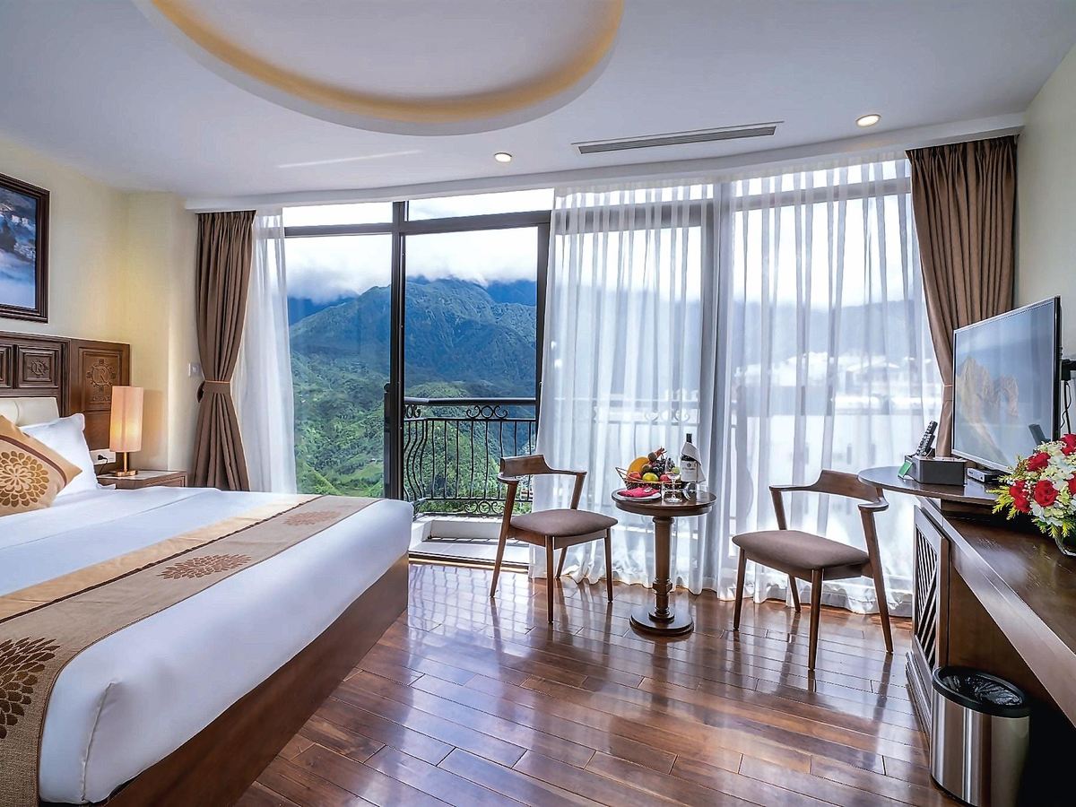 Double bed on a wooden floor beside floor-to-ceiling windows, with a balcony looking over green mountains