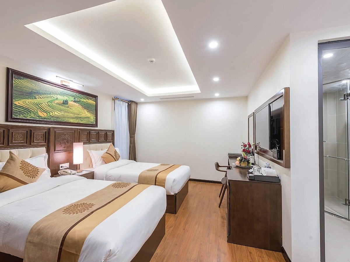 Room with two beds under carved wooden headboards, a writing desk and a glass shower cubicle