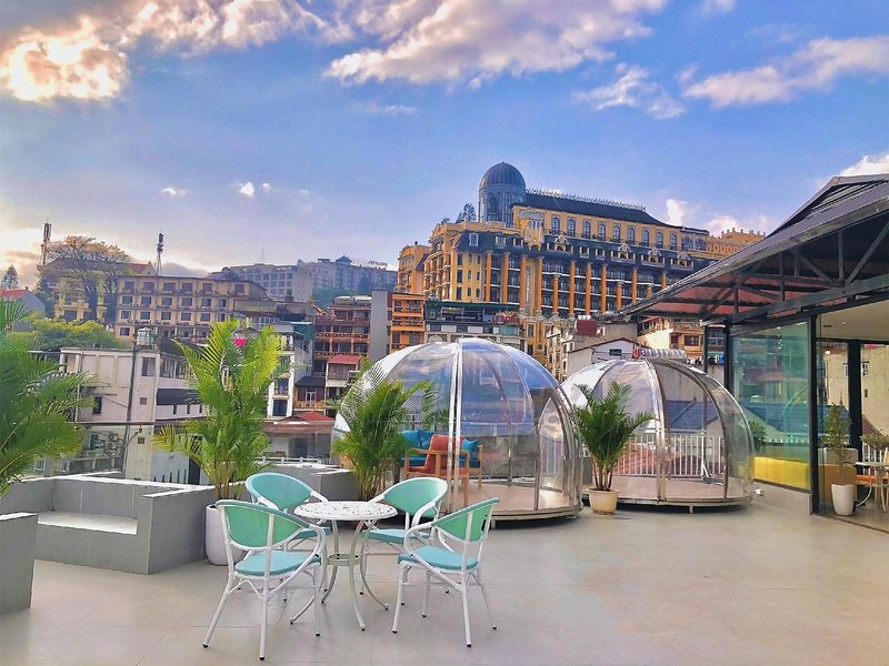 Rooftop terrace with two clear glass domes, mint-green chairs and potted palms above the rooftops of a hill town